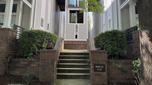 Un edificio con entrada central, flanqueada por escalones de ladrillo y follaje, y un cartel que dice 