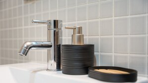 Ein Badezimmerwaschbecken mit chromfarbenem Wasserhahn, einem schwarzen Seifenspender und einer schwarzen Seifenschale.