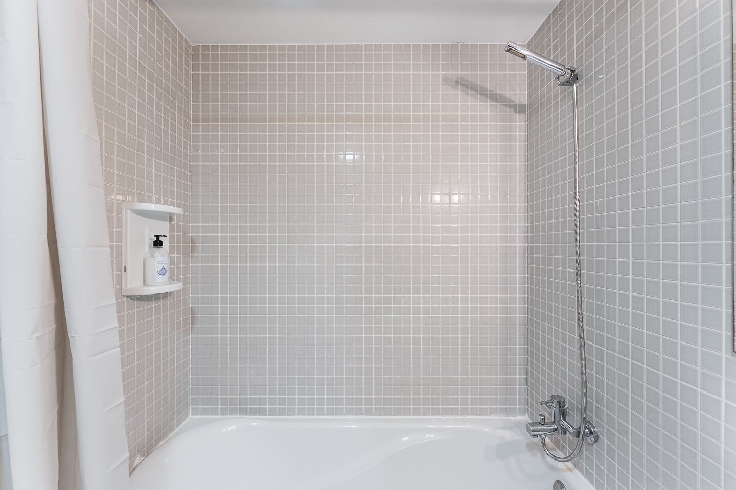 A bathroom with a bathtub, a shower, and a hand soap dispenser on the wall.
