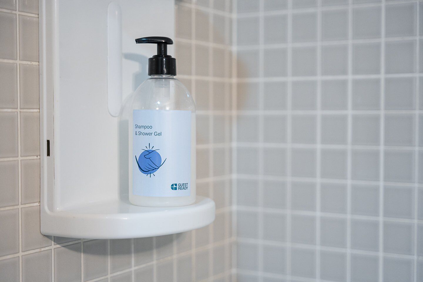 Un baño con un lavabo blanco y una botella de champú y gel de ducha sobre la encimera.