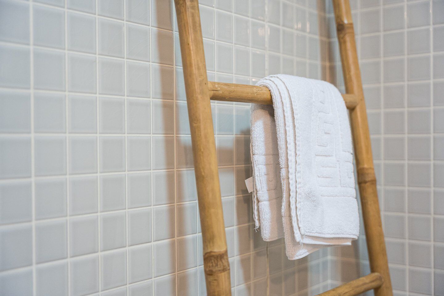 Una escalera de madera apoyada contra una pared de azulejos, con una toalla blanca colgada.