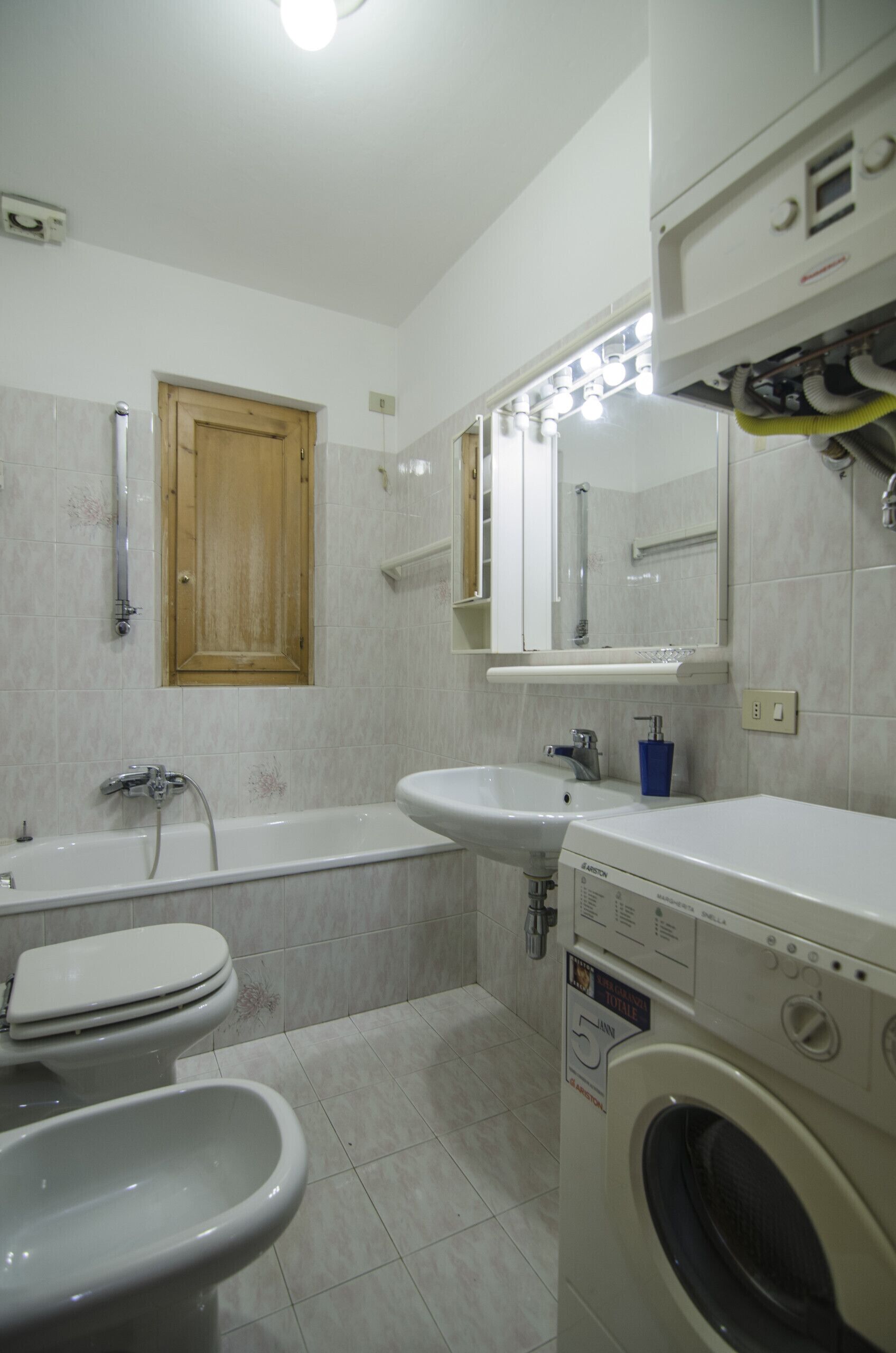 A bathroom with a bathtub, toilet, bidet, sink, and washing machine.