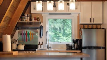 A modern kitchen with a wooden ceiling, white cabinets, a stainless steel refrigerator, and a window with a view of greenery.