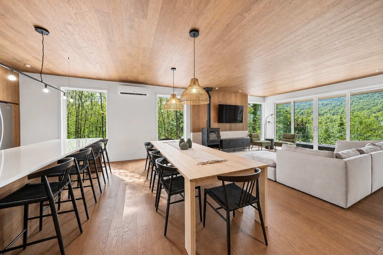 A modern kitchen with a dining area, large windows, and a view of greenery.