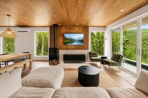 A modern living room with a fireplace, large windows, and a view of the outdoors. - Mountain | Sauna | Camp de base du Massif (Saint-Philémon)