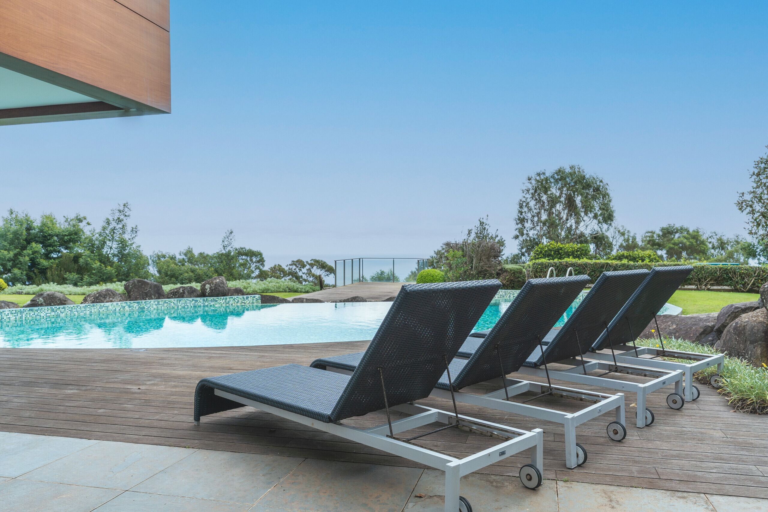 Zona de piscina con sillones de descanso y una terraza de madera.