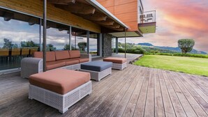 Un espacio exterior moderno con mobiliario de mimbre, una terraza de madera y vistas al paisaje.