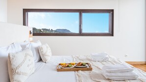Un dormitorio con cama, almohadas, una bandeja con croissants, jugo de naranja y vista a la montaña a través de una ventana.