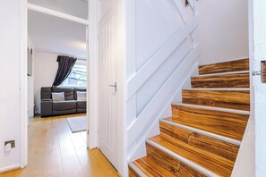 Eine Treppe mit Holzboden und weißen Geländern führt zu einem Raum, der ein graues Sofa und ein Fenster mit Vorhängen beinhaltet.