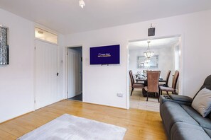 Ein modernes Wohnzimmer mit einem grauen Sofa, einem weißen Teppich und einem Essbereich mit Holzsesseln und einer Chandelier.
