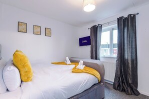 Ein Hotelzimmer mit einem Bett, einem Fenster mit Vorhängen und drei gerahmten Bildern an der Wand.