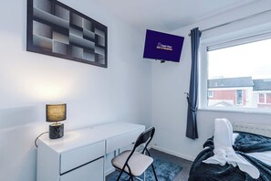 A bedroom with a bed, a desk, a chair, a TV, and a window with curtains. - M24 | Spacious 4BR House | Parking | City Centre (Middleton)
