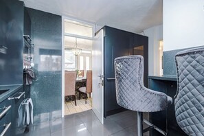 A modern kitchen with a dark backsplash, a dining area with a chandelier, and a door leading to a room with a wooden floor. - M24 | Spacious 4BR House | Parking | City Centre (Middleton)