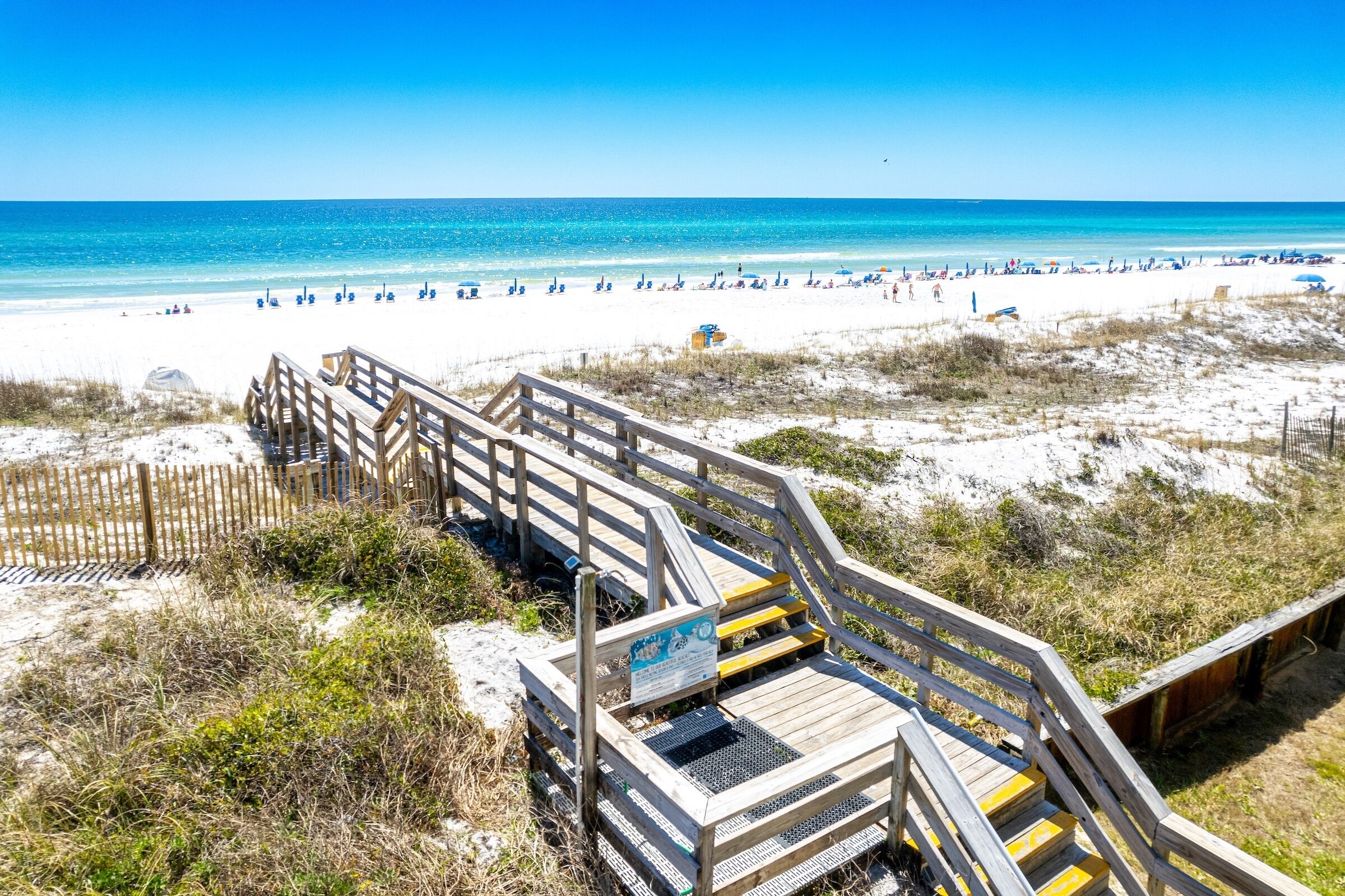 A wooden boardwalk leading to a beach with clear skies and calm waters.
