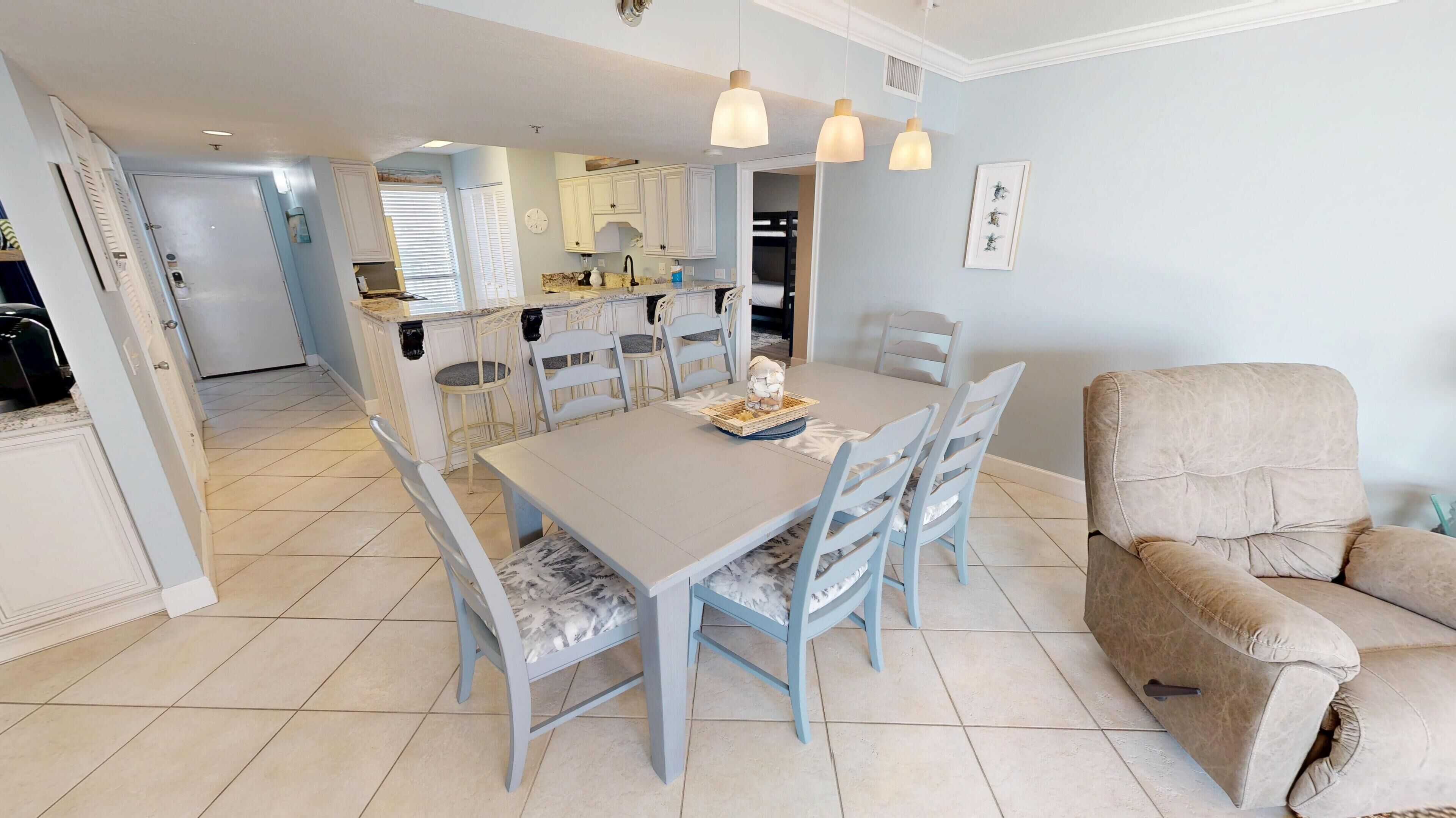 Un comedor con una mesa y sillas, una cocina al fondo y un sillón color beige.