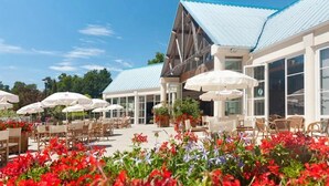 Un bâtiment avec un toit bleu, des tables et chaises à l’extérieur sous des parasols blancs, et des fleurs rouges au premier plan.