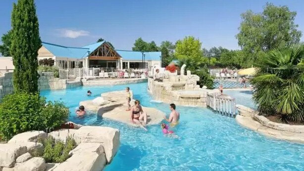 Un espace piscine doté de plusieurs éléments aquatiques et d’un bâtiment en arrière-plan.