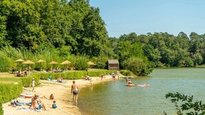 Une plage au bord de la rivière où l’on peut voir des gens se détendre, des parasols et des bateaux.