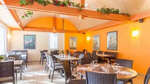Un restaurant doté de nombreuses tables et chaises, d’un sol carrelé et d’un plafond haut orné de plantes décoratives.