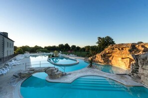 Zona de piscina con varias piscinas, sillas de descanso y un paisaje rocoso.