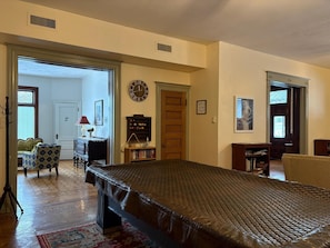 A room with a large bed, a wooden door, a wall clock, a bookshelf, and a chair.
