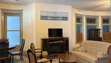 A living room with a fireplace, a television, a sofa, and a dining area with chairs and a table.