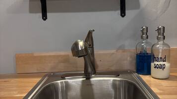 Un lavamanos de cocina con un grifo moderno, un estante de madera arriba con una cafetera, un vaso medidor y una caja de Pyrex.