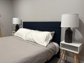 Ein ordentlich bezogenes Bett mit einer gemusterten Tagesdecke, einem dunklen Kopfteil und zwei Nachttischen mit Lampen.