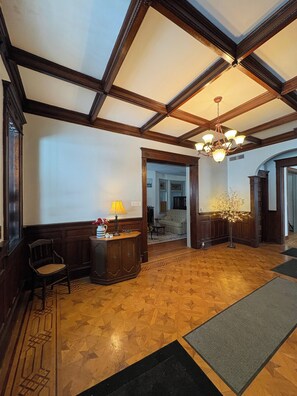 A lobby with a wooden floor, a reception desk, a chandelier, and a door leading to another room.