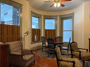 A room with a curved ceiling, wooden shutters, a dining table with chairs, and a patterned armchair. - NH5: Charming 1BR in Historic Home (DuBois)