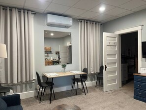 A room with a dining table, chairs, a mirror, an air conditioning unit, and a wardrobe.
