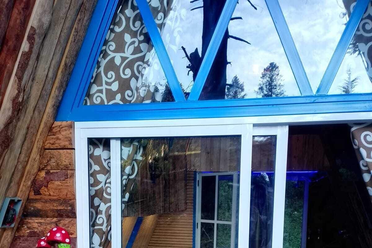 Una cabaña de madera acogedora con un ventanal de vidrio que da a un dormitorio con cama y ventana.