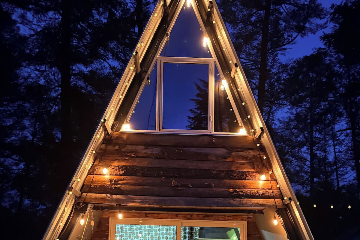 Una cabaña de madera con techo triangular, puerta de vidrio y luces colgantes.