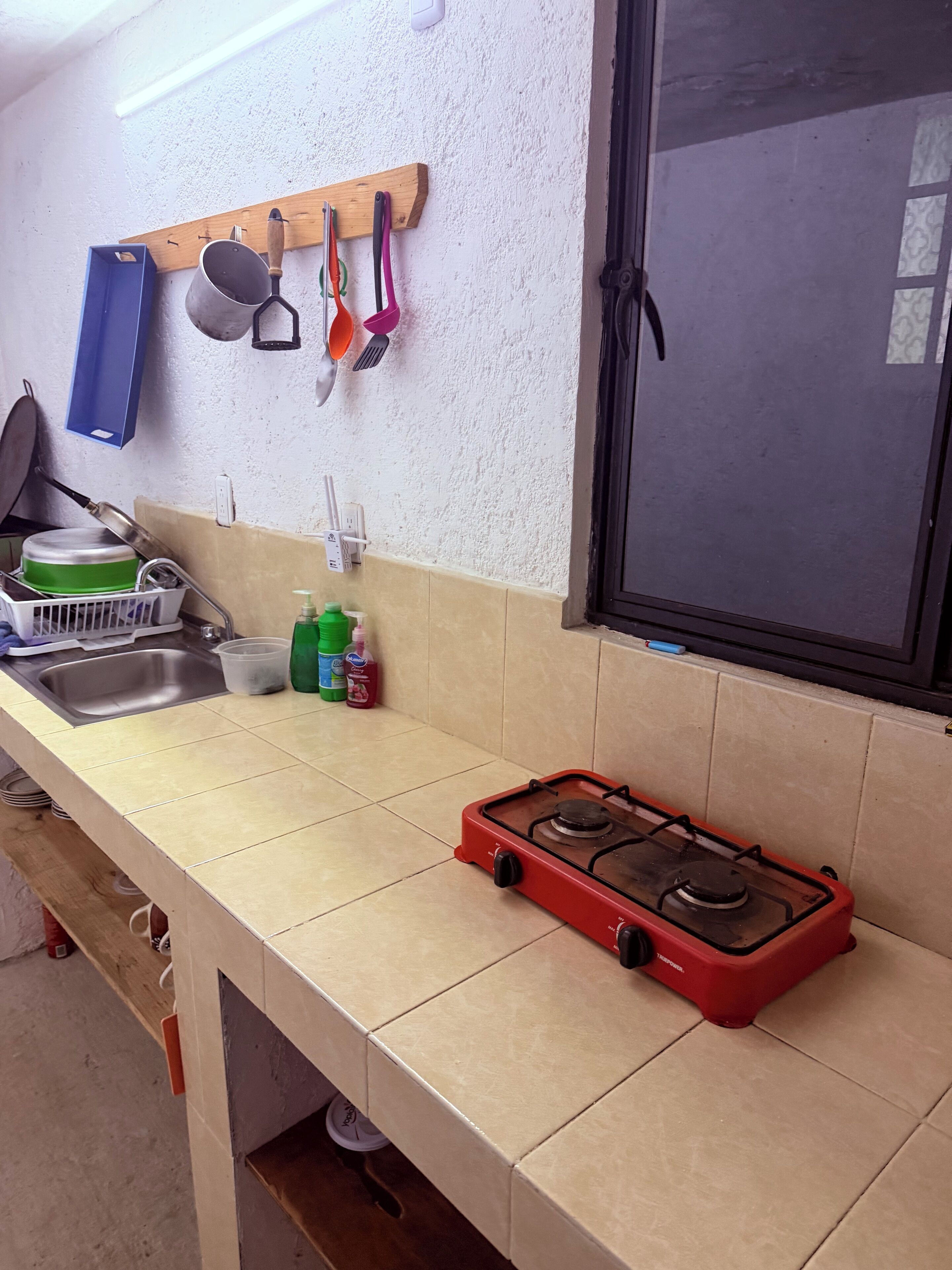 A kitchen with a gas stove, a sink, and various utensils hanging on the wall.