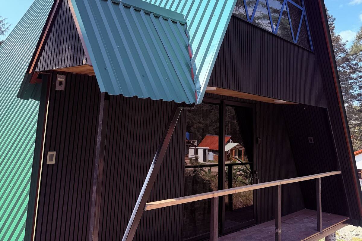 Un edificio moderno con techo triangular, terraza de madera y revestimiento de metal.