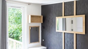 Una camera d'albergo moderna con un letto, una scrivania, uno specchio e un'ampia finestra.