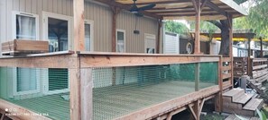 Eine Holzterrasse mit einem Netzabschluss, Holzgeländern und einem überdachten Bereich mit Deckenventilator.