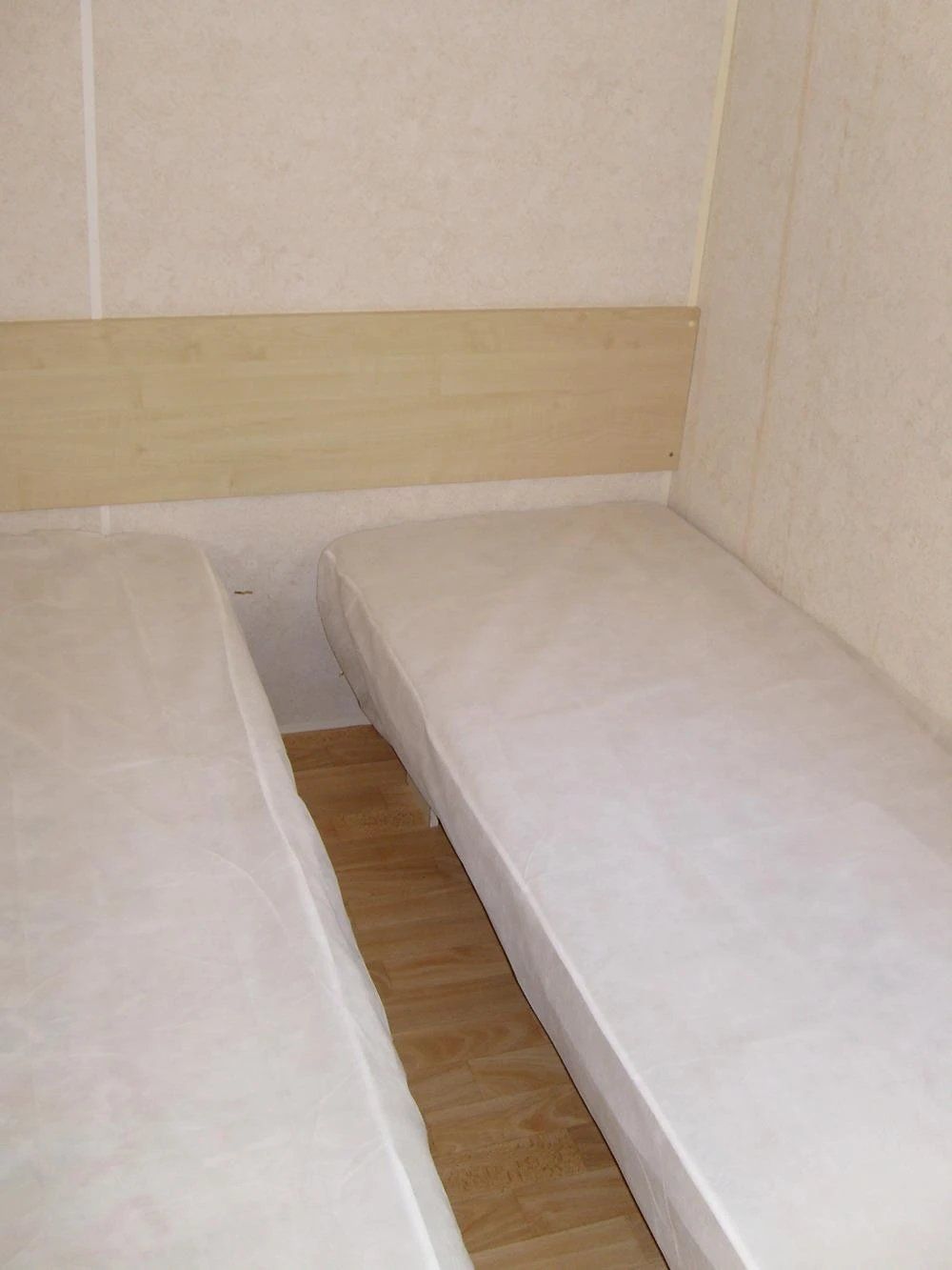 Een kleine kamer met een enkel bed, een houten vloer en een effen, lichtgekleurde muur.