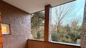 Ein Zimmer mit Backsteinwand, einem Fenster mit Blick auf Bäume und einem Fliesenboden.