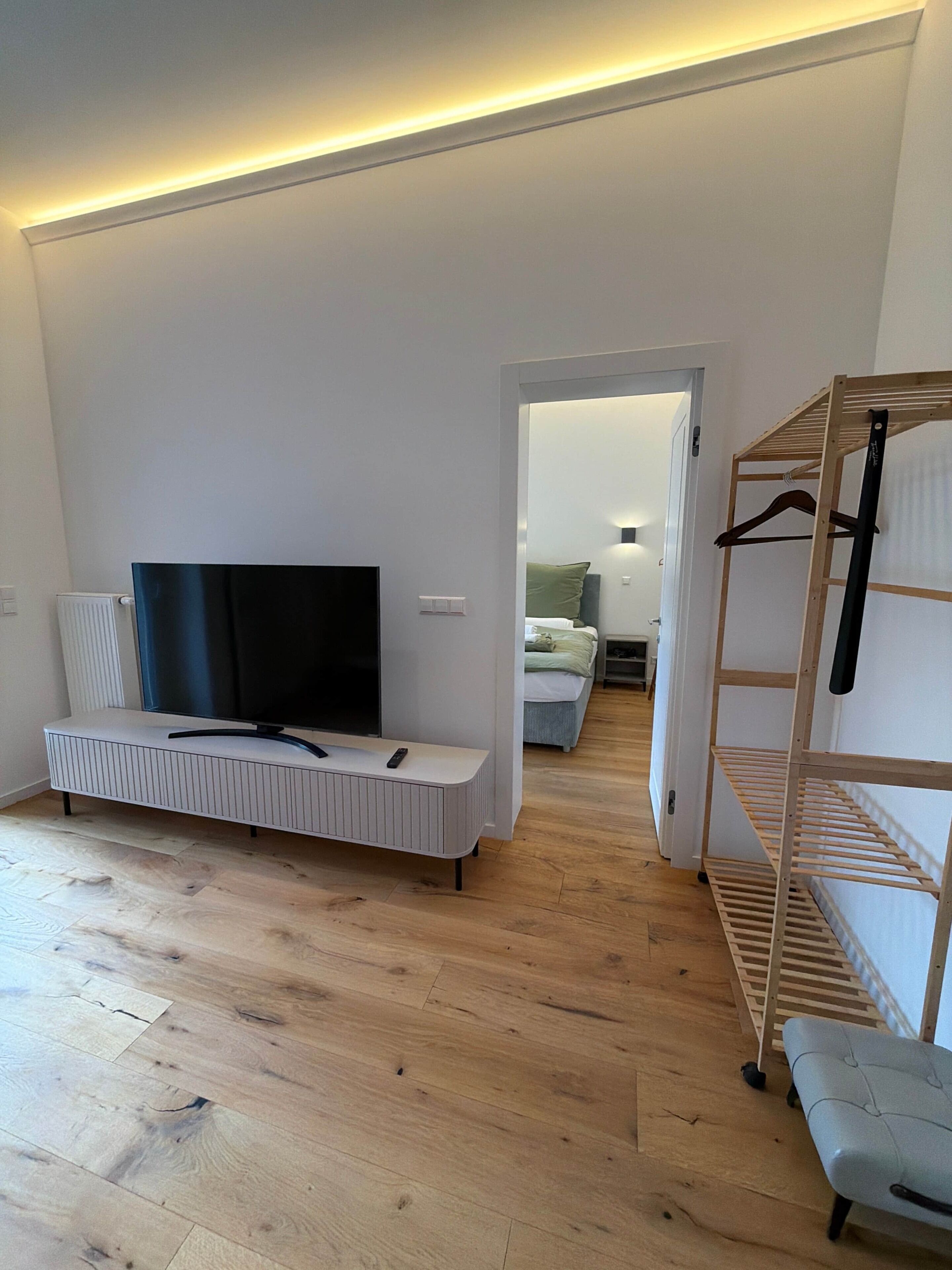 En moderne stue med et fladskærms-tv, en bænk, trægulv og et walk-in closet med hylder.