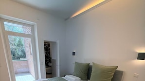 Ein modernes Schlafzimmer mit einem großen Bett, einem Nachttisch, einer eingebauten Ablage und Blick durch eine offene Tür.