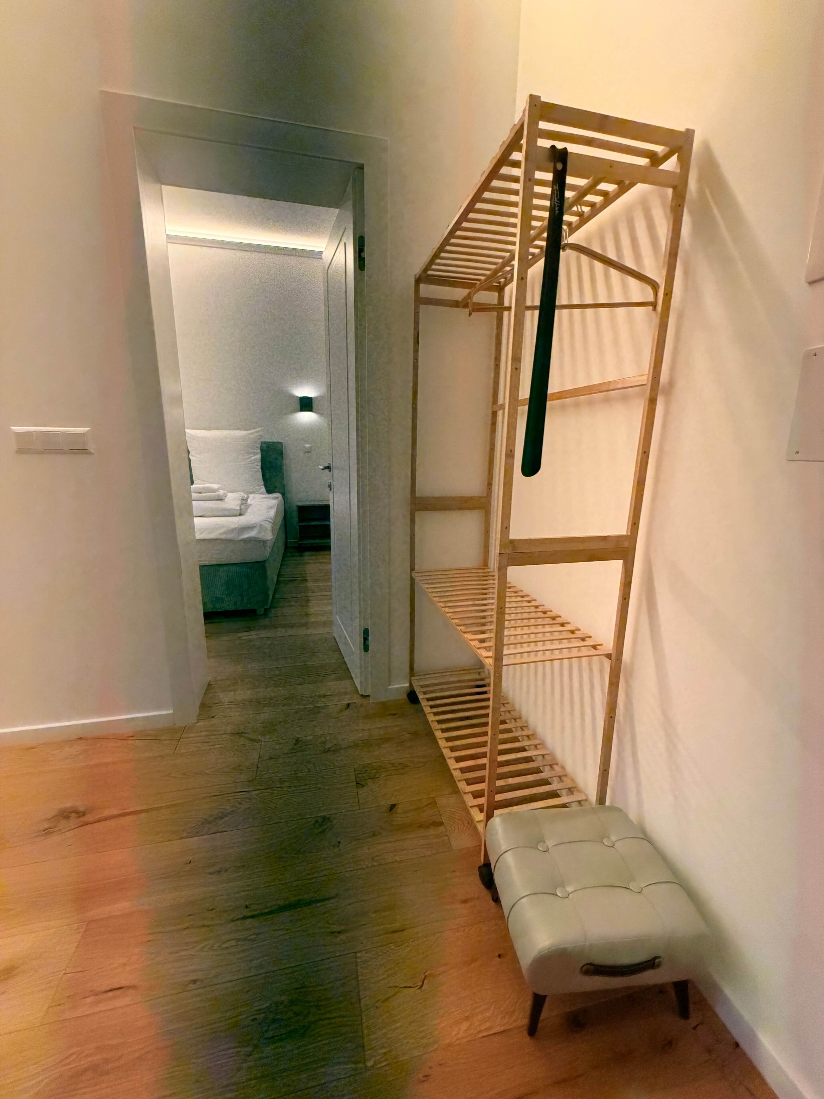 Ein schmaler Flur mit einer hölzernen Bank und einem Etagenbett mit einer Leiter. Eine Tür führt zu einem Zimmer mit einem Bett und einem Nachttisch.