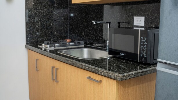 Una cocina con armarios de madera, encimera de granito, pileta, microondas y refrigerador.
