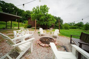 A covered outdoor seating area with Adirondack chairs, a fire pit, and a wooden deck. - The Arcade | Hocking Hills, Hot Tub, Firepit (Logan)