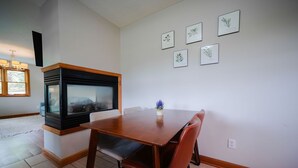 Een eetgedeelte met een houten tafel en stoelen, een open haard en ingelijste botanische prints aan de muur.