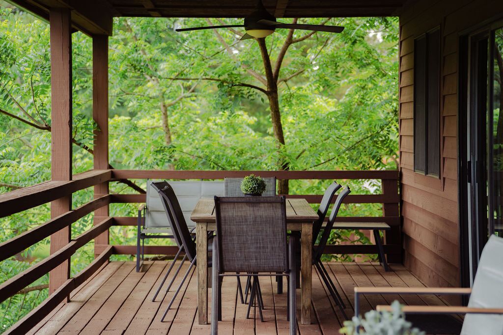 Een houten terras met een tafel en stoelen, omringd door een leuning, met uitzicht op een weelderig groen bos.