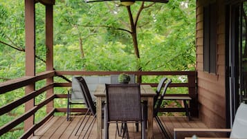 Een houten terras met een tafel en stoelen, omringd door een leuning, met uitzicht op een weelderig groen bos.