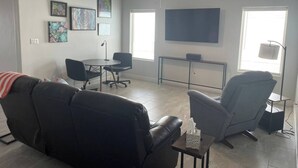 A living room with a black leather sofa, gray armchairs, a small table, and a TV mounted on the wall. - Desert Retreat - Relax and Enjoy (Las Cruces)