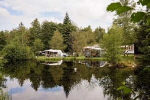 A lakeside campsite with RVs and cabins, surrounded by dense trees and a calm lake.