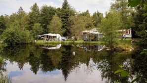 Campeggio sul lago con camper e cabine, immerso in una fitta vegetazione e affacciato su un lago tranquillo.